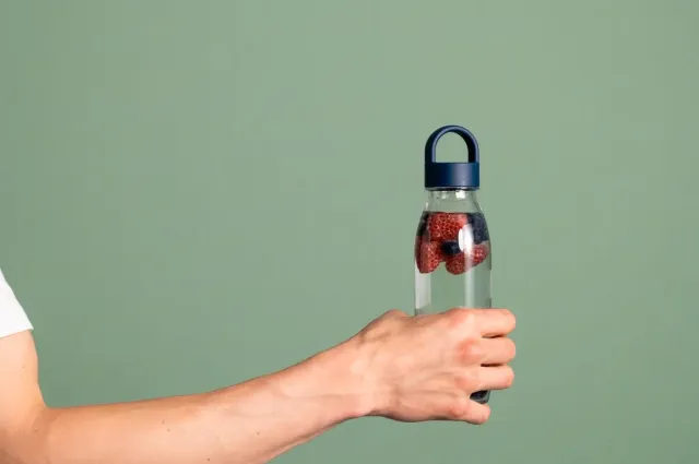 Man houdt een waterfles vast met daarin water en rood fruit